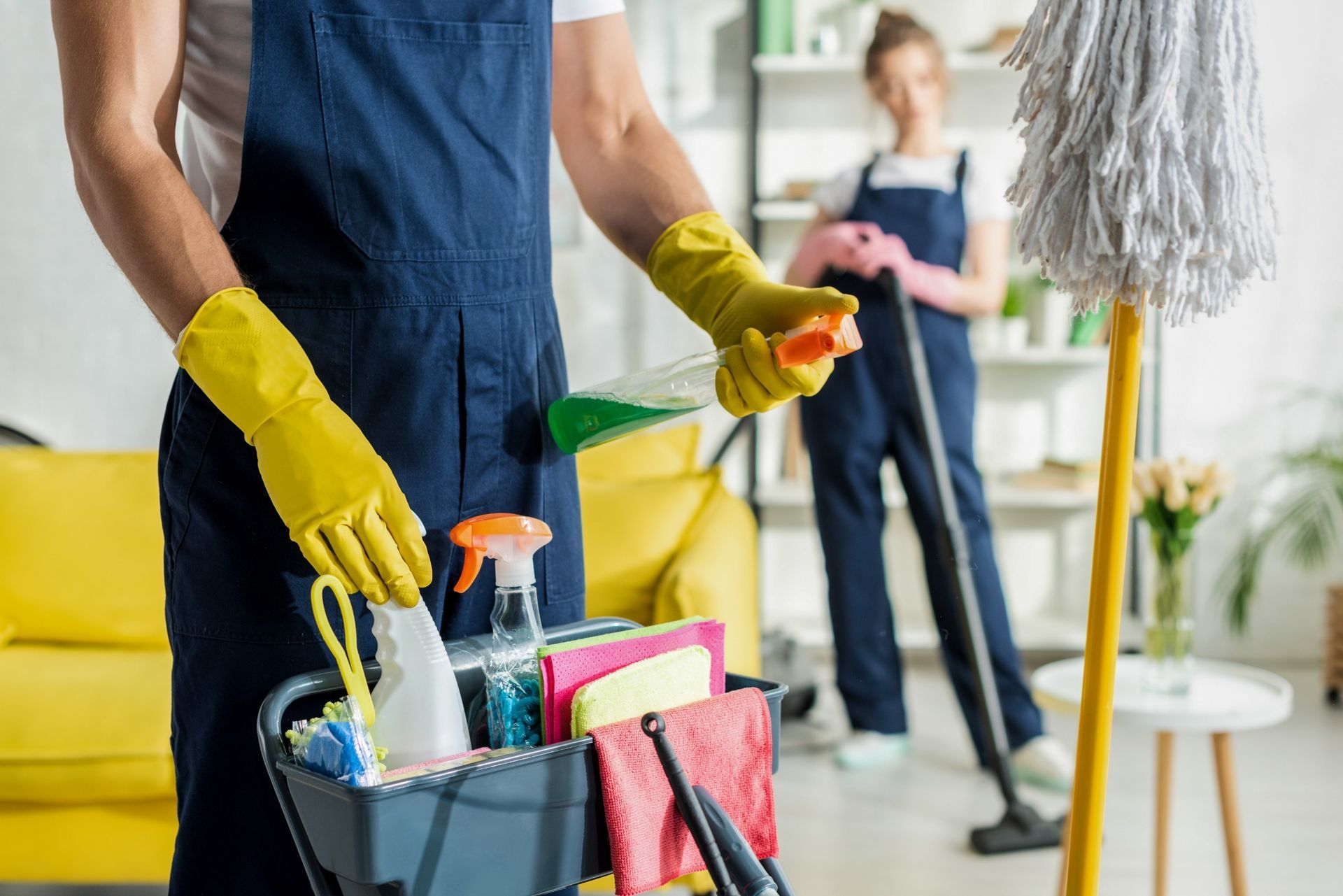 Un hombre sostiene un balde de productos de limpieza en una sala de estar.